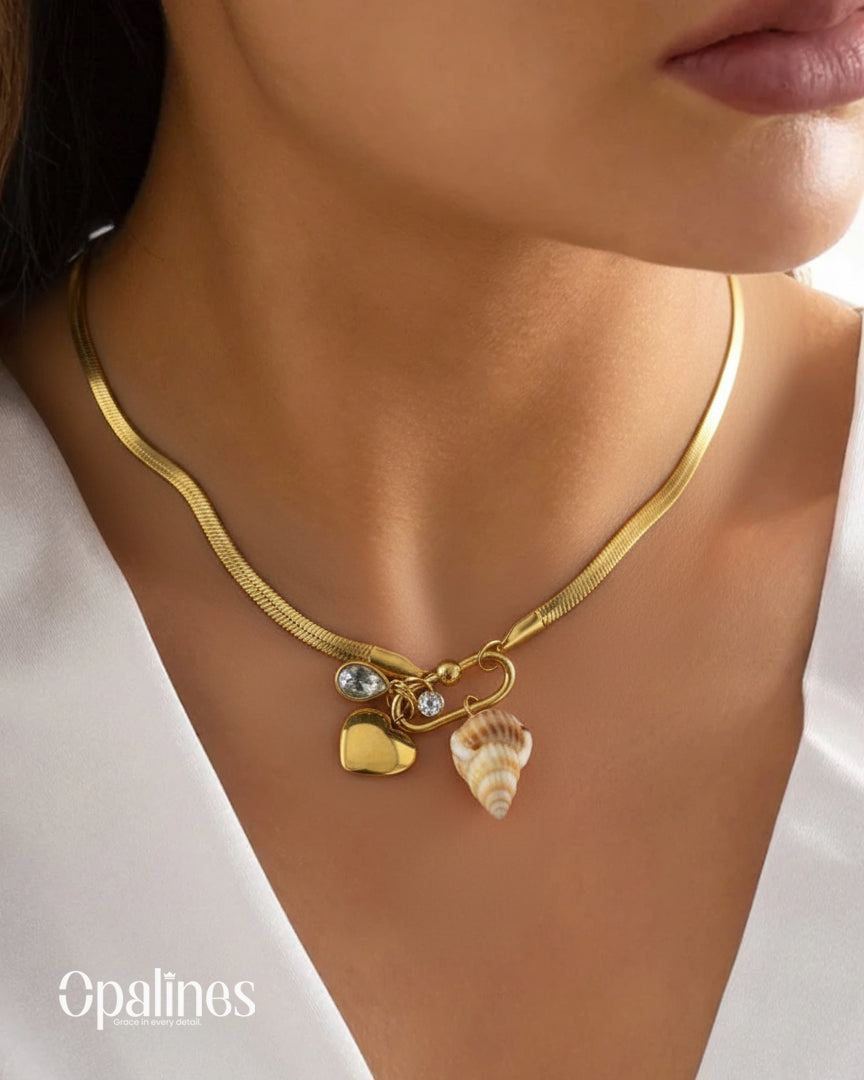 stunning gold necklace from Opalines features a heart-shaped locket, a diamond accent, and a seashell charm