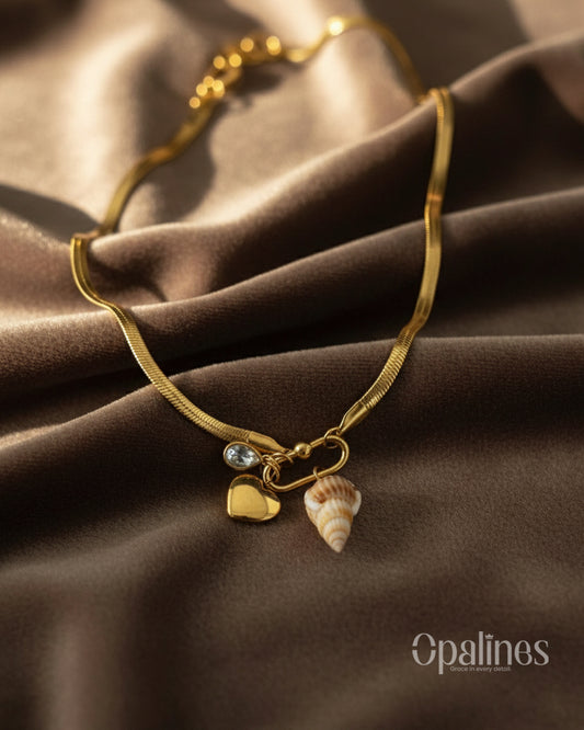 stunning gold necklace from Opalines features a heart-shaped locket, a diamond accent, and a seashell charm